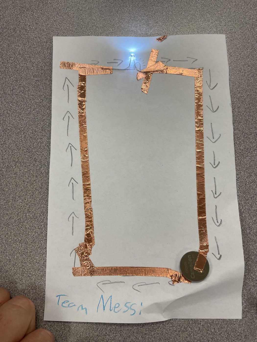 A paper circuit made with copper tape and a coin battery lighting a small LED, built by students