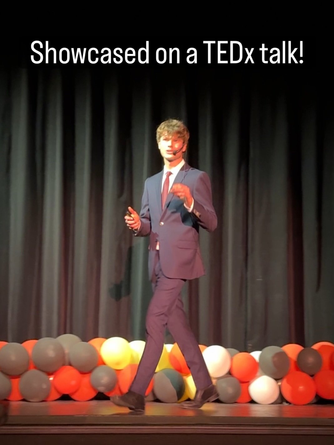 A STEMroots founder speaking on a TEDx stage, with a row of balloons along the front of the stage
